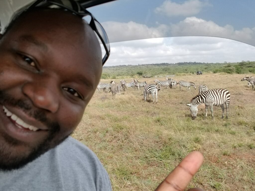 Safari traveler smiling near a grassy plain where zebras are grazing